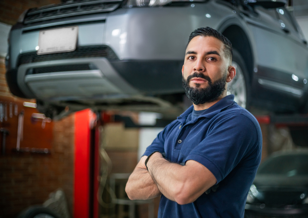 man with arms crossed, wearing polo shirt, standing near car lift